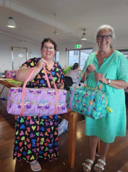 Two Women Are Standing Next to Each Other Holding Bags and Smiling — Lyn-Jelle Crafts in Emu Park, QLD