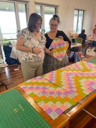 Two Women Are Looking at a Quilt on a Table — Lyn-Jelle Crafts in Emu Park, QLD