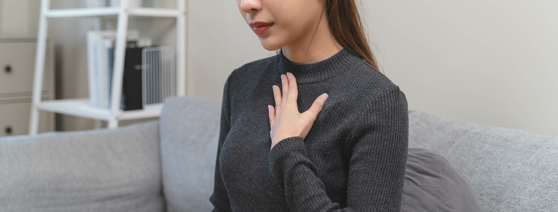 A woman is sitting on a couch with her hand on her chest.