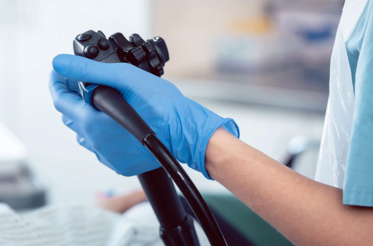 A person wearing blue gloves is holding an endoscope.