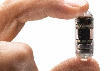 A person is holding a small capsule in their hand.