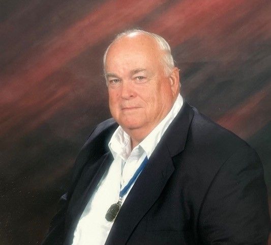 A man in a suit and tie is sitting in front of a red background.