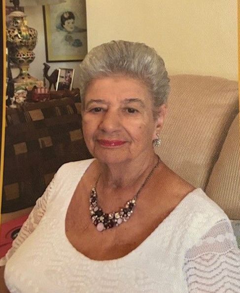 A woman wearing a white shirt and a necklace is sitting in a chair