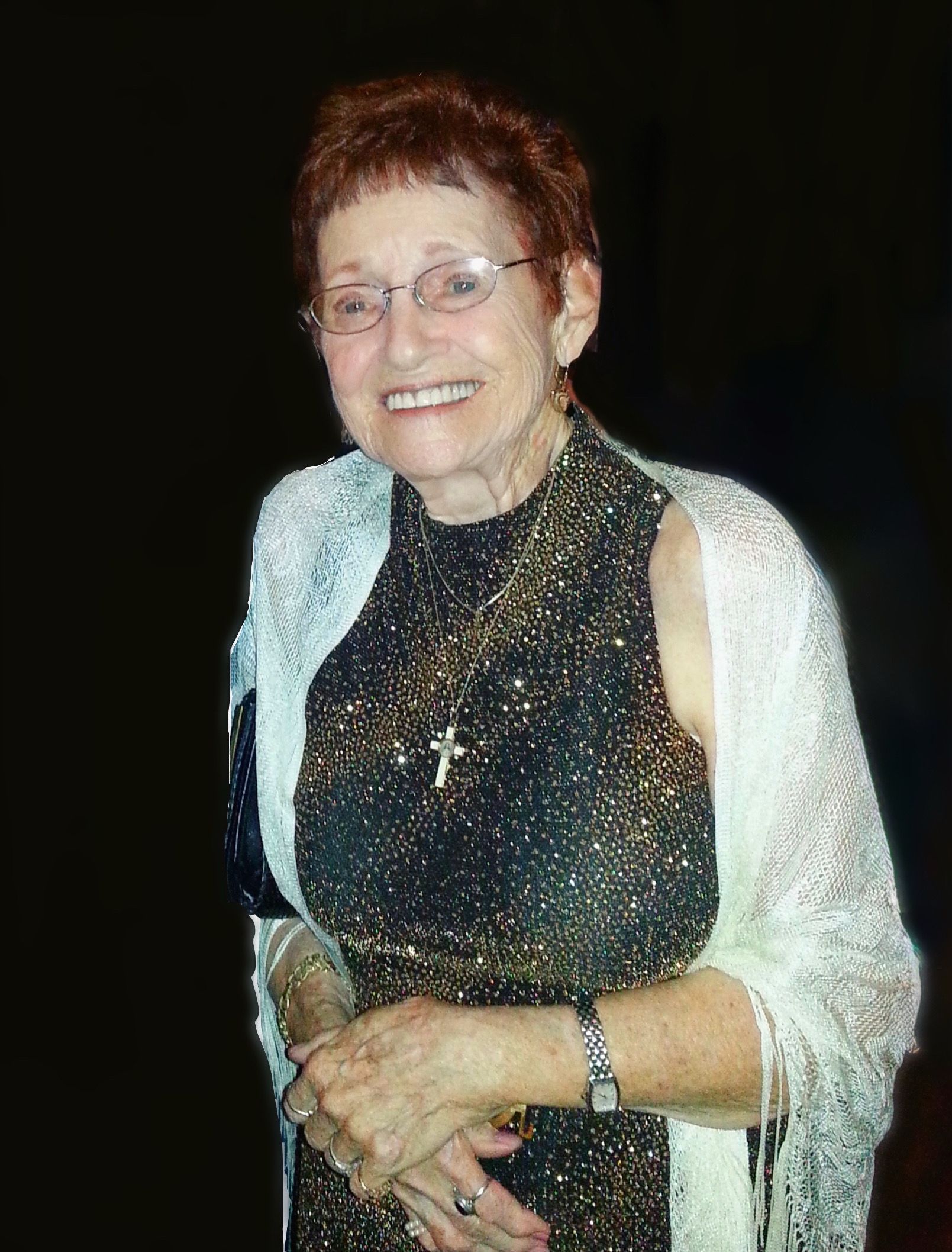 An elderly woman wearing a black and gold dress and a white shawl is smiling.