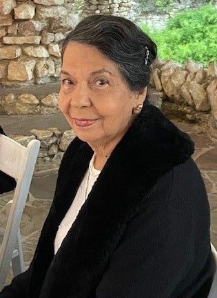 A woman in a black coat and white shirt is sitting in a chair.