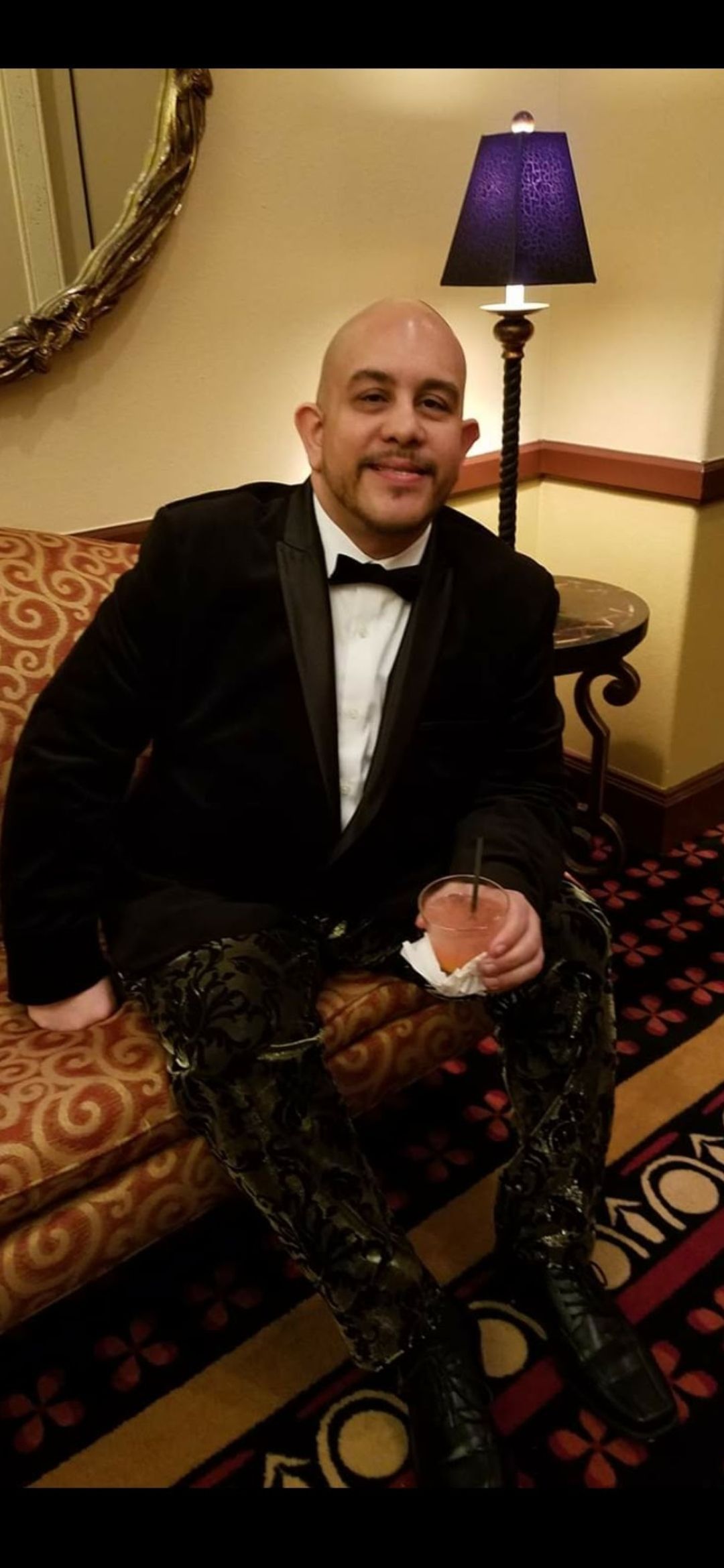 A man in a tuxedo is sitting on a couch next to a lamp.