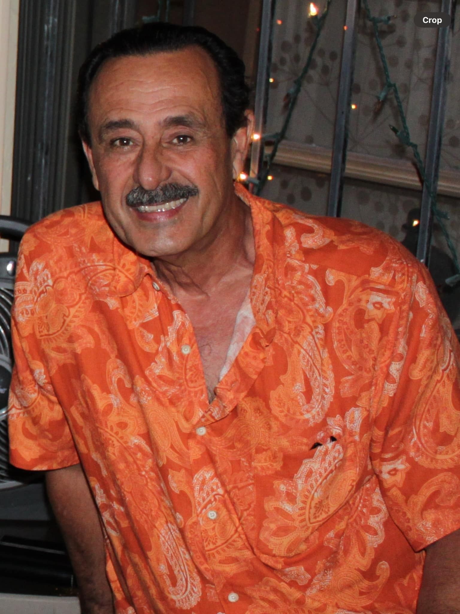 A man with a mustache is wearing an orange shirt and smiling.