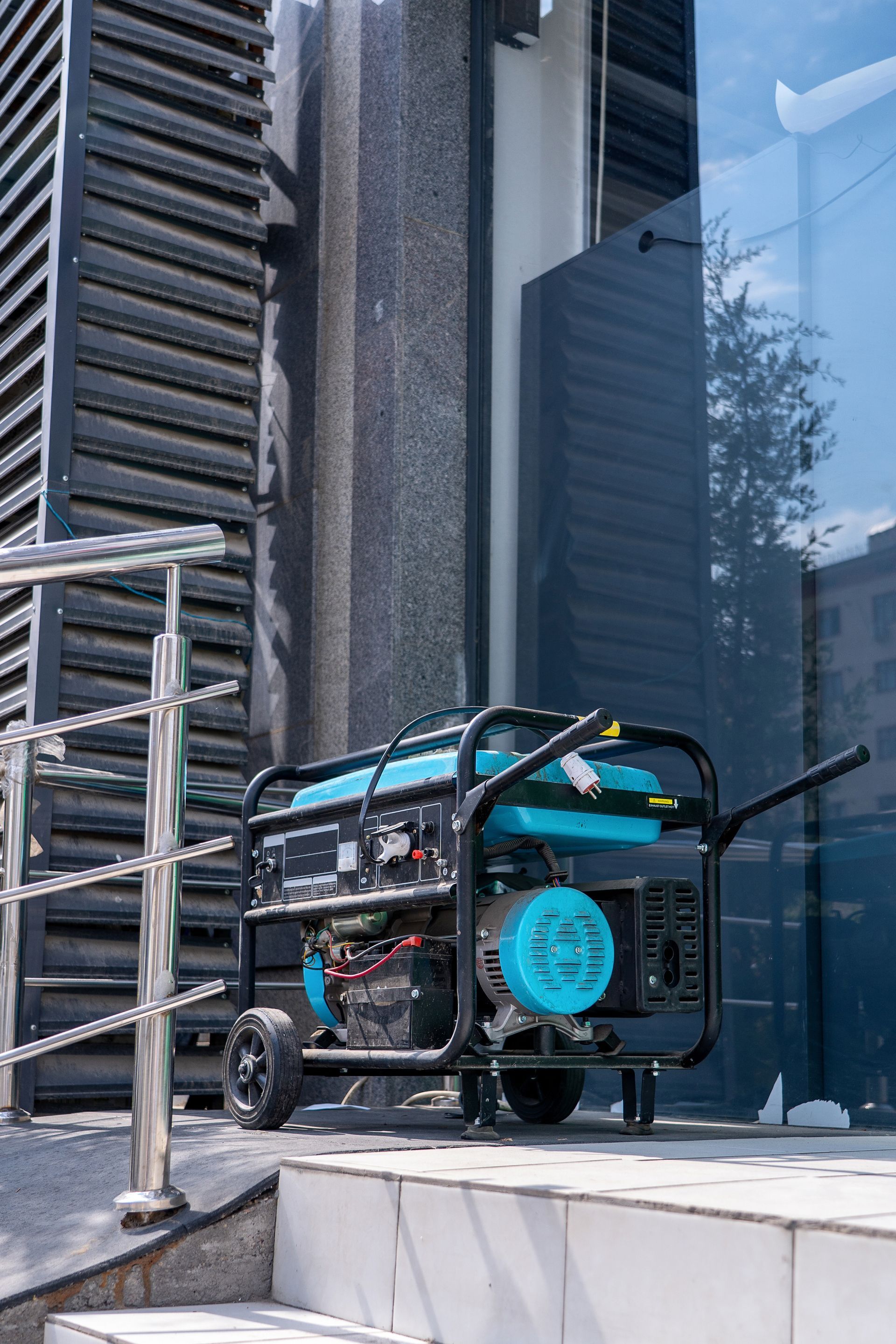 Portable generator on a sidewalk beside a glass building and metal railing