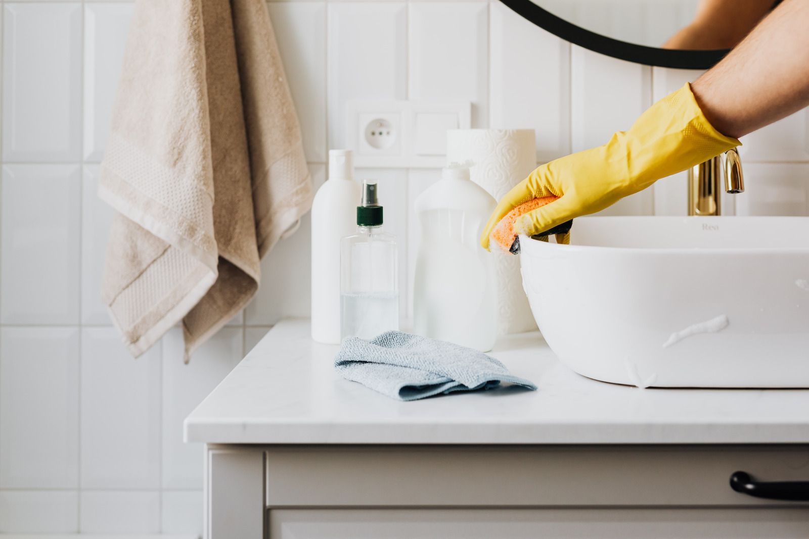Person with yellow gloves cleaning a white bathroom sink with a sponge.