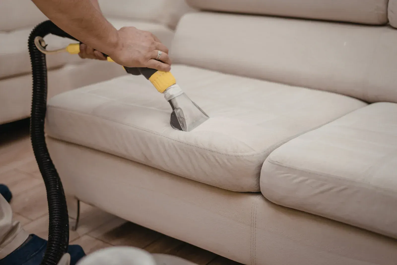 A person uses an industrial steam vacuum cleaner to deep clean a light-colored fabric sofa.