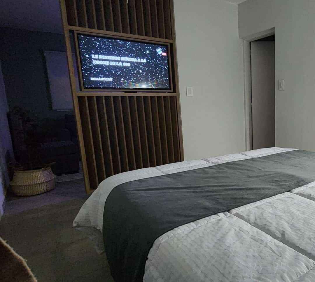 Dormitorio con cama, TV sobre panel de madera y vista a otra habitación.