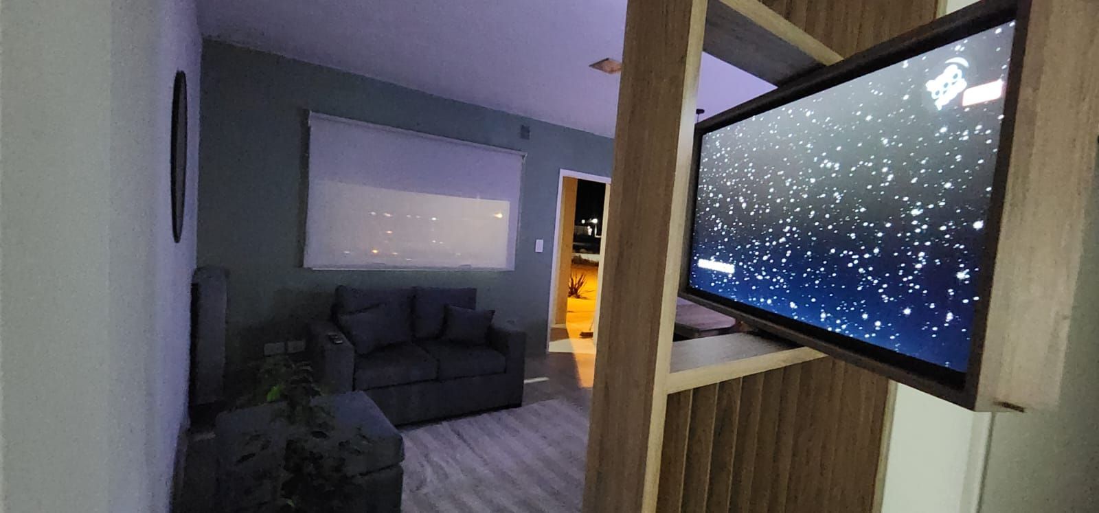 Sala de estar con televisor que muestra una escena nocturna estrellada, sofá y una puerta a otra habitación.