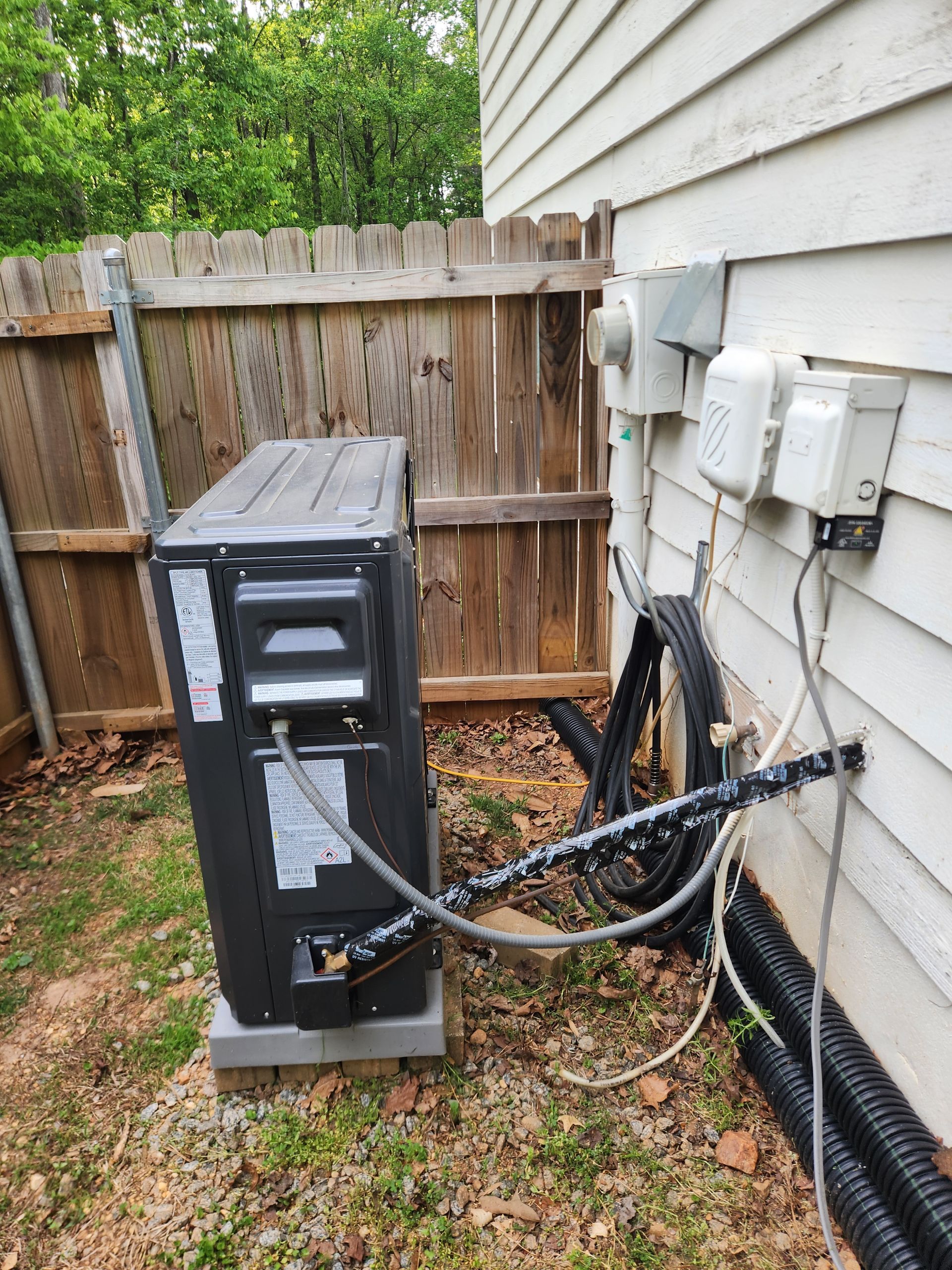 Outdoor HVAC unit beside a house, with exposed wires and utility meters on the wall.