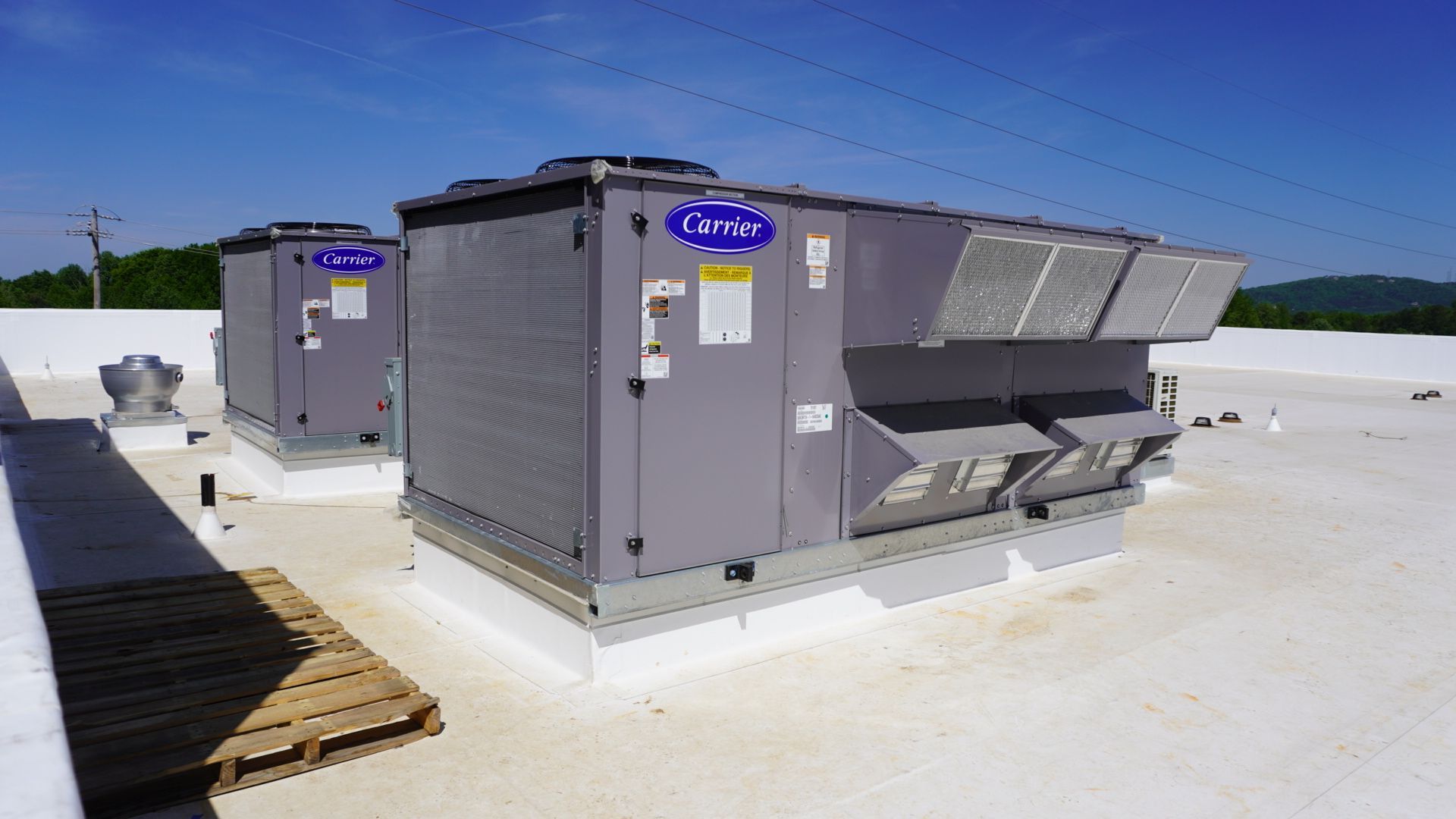 Large rooftop HVAC units on a flat white roof, with gray metal panels and vents.