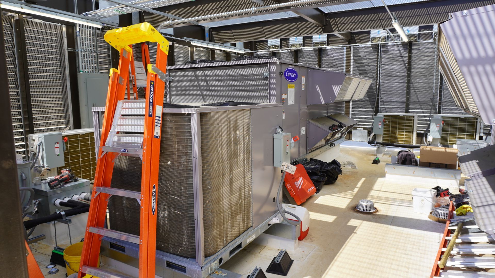 Industrial worksite with orange ladders, large equipment crates, and tools inside a metal structure