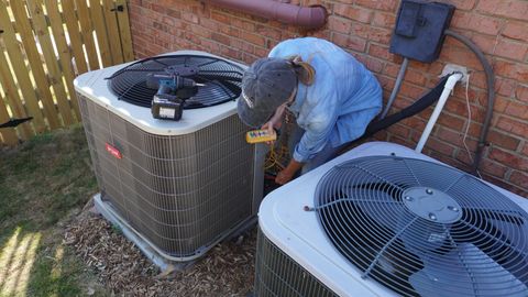 Technician servicing outdoor HVAC unit beside a brick house and wooden fence
