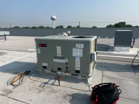 Large rooftop HVAC unit with hoses and tools on a flat commercial roof.