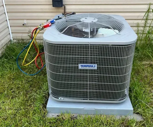 Outdoor air conditioner unit beside a house with colorful service hoses attached