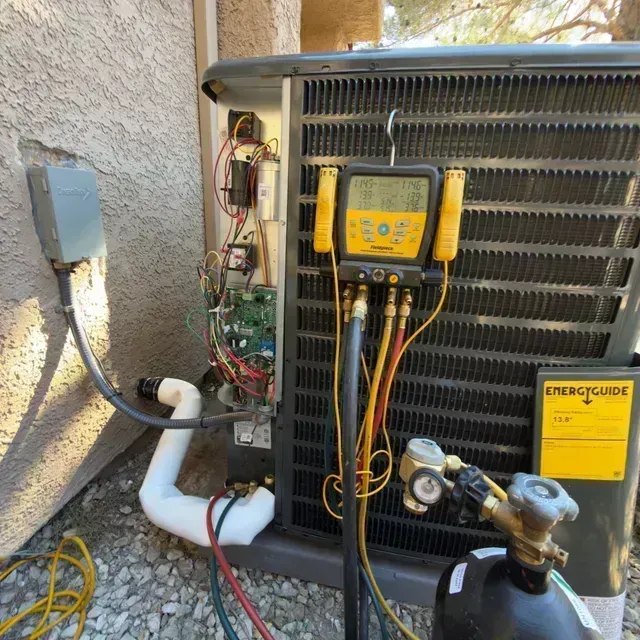HVAC unit with yellow digital gauges and exposed wiring beside a stucco wall