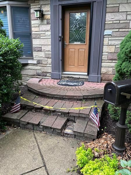 Damaged brick steps leading to a front door, flagged with caution tape and American flags.