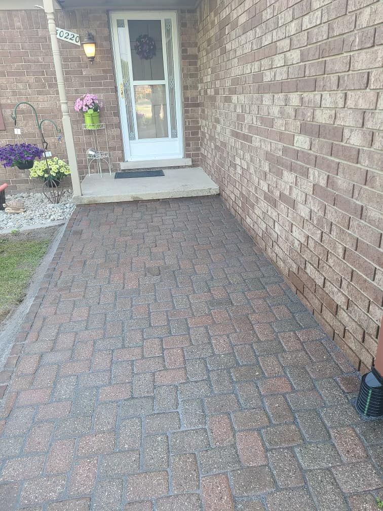 Brick walkway leading to a white door. Brick wall on the right. Flower pots sit to the left.