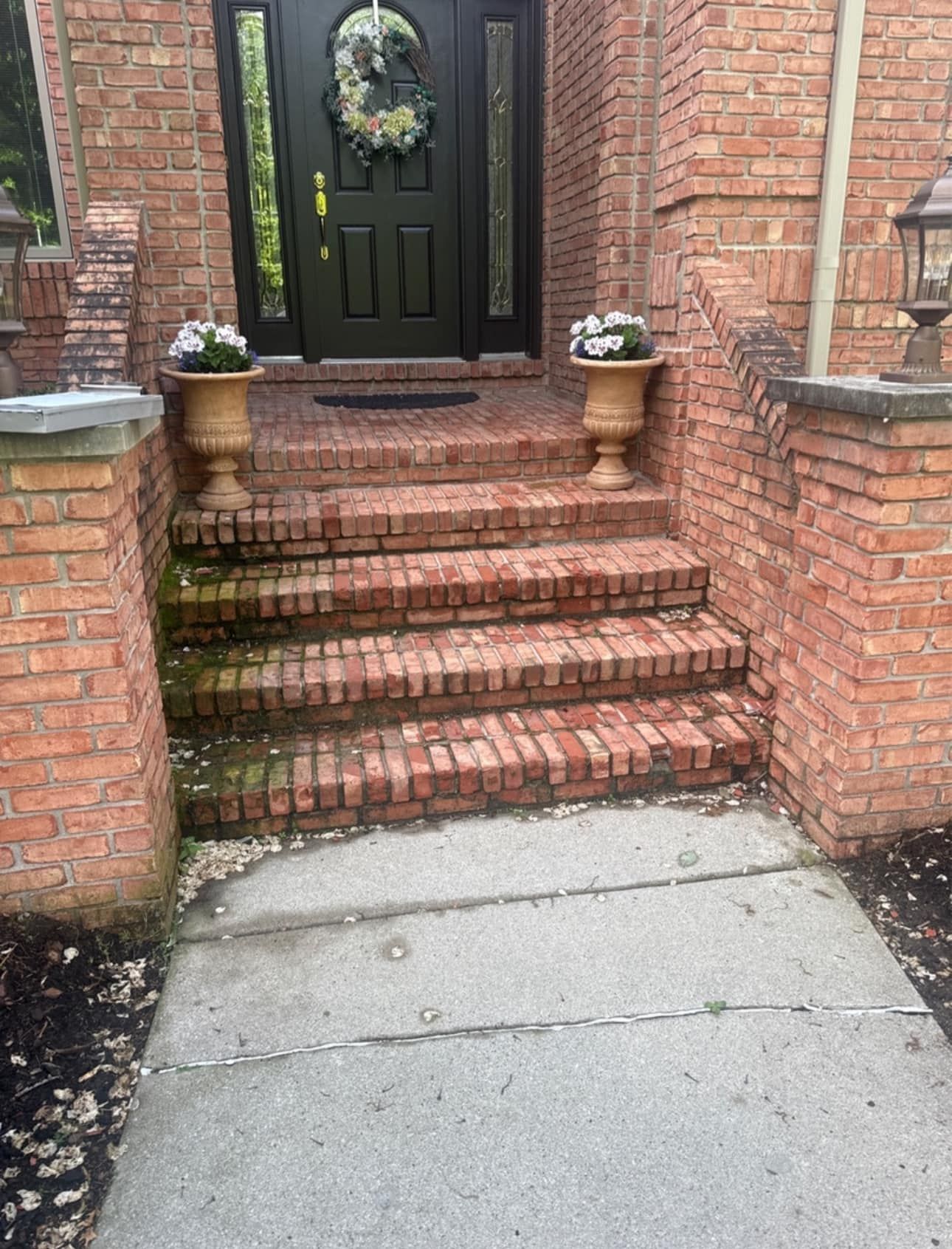 Brick steps lead up to a dark front door with urns, with a sidewalk approach.