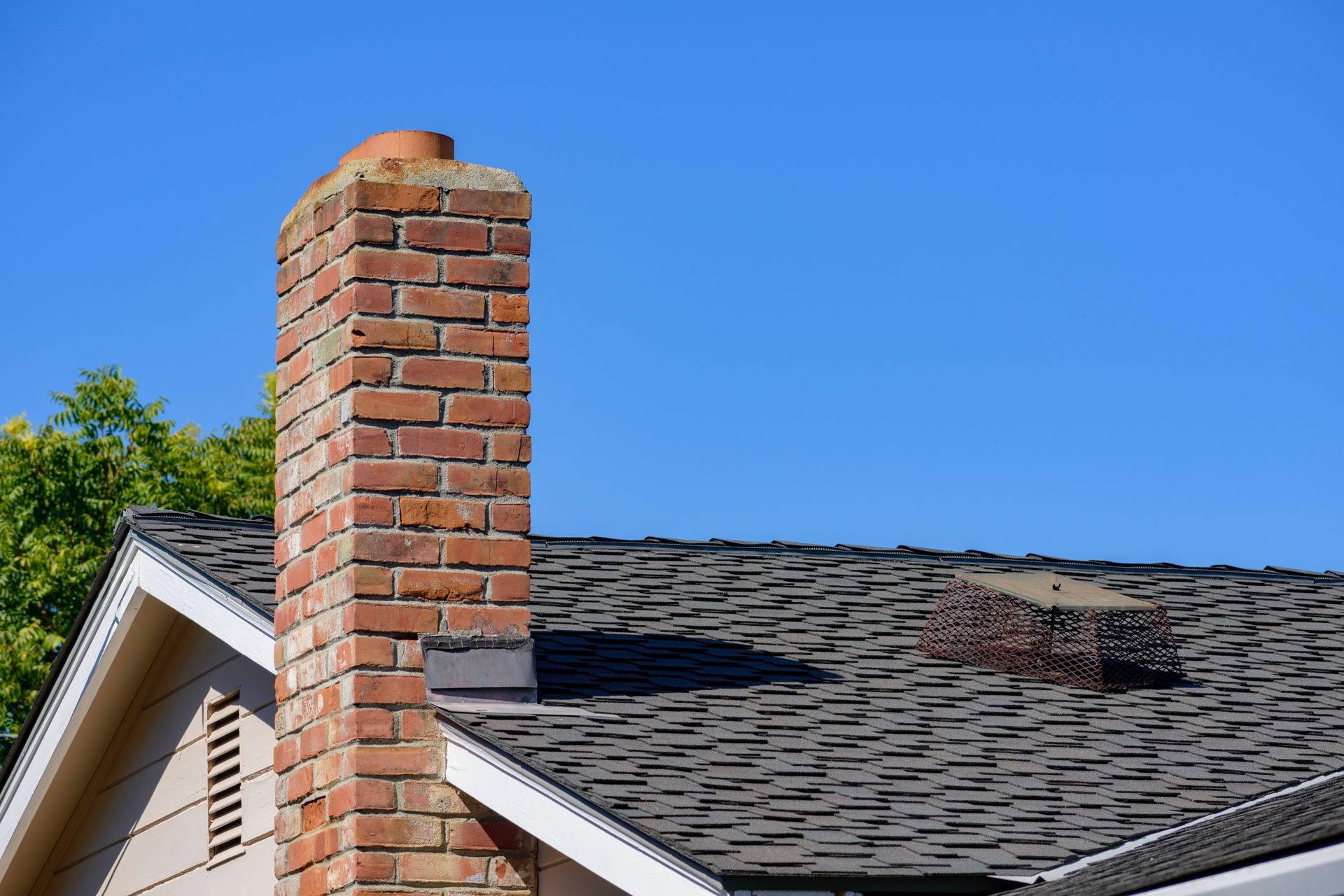 Brick chimney on a residential home against a clear blue sky.