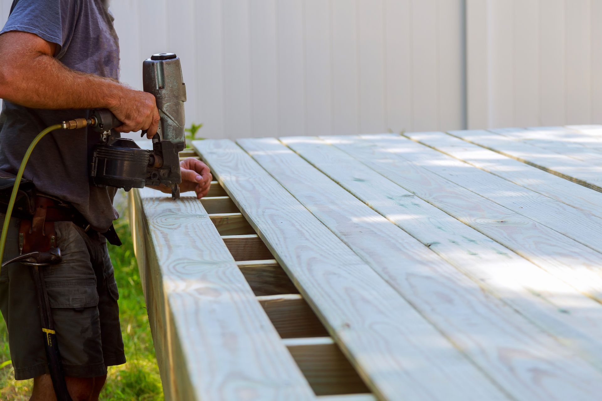 Worker building a backyard deck, putting up a nail gun.