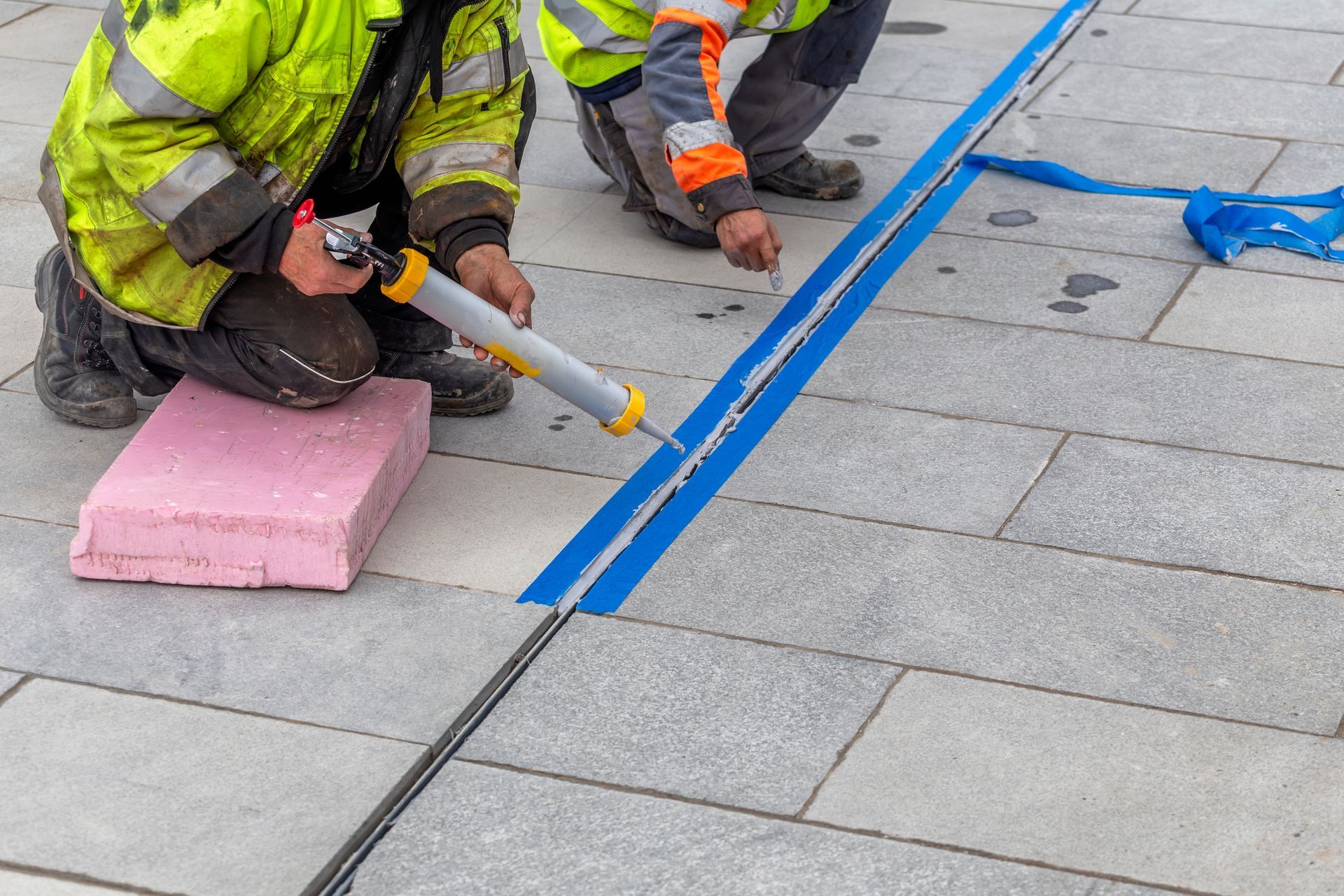 Workers sealing roof seams with blue tape and caulk on a flat rooftop