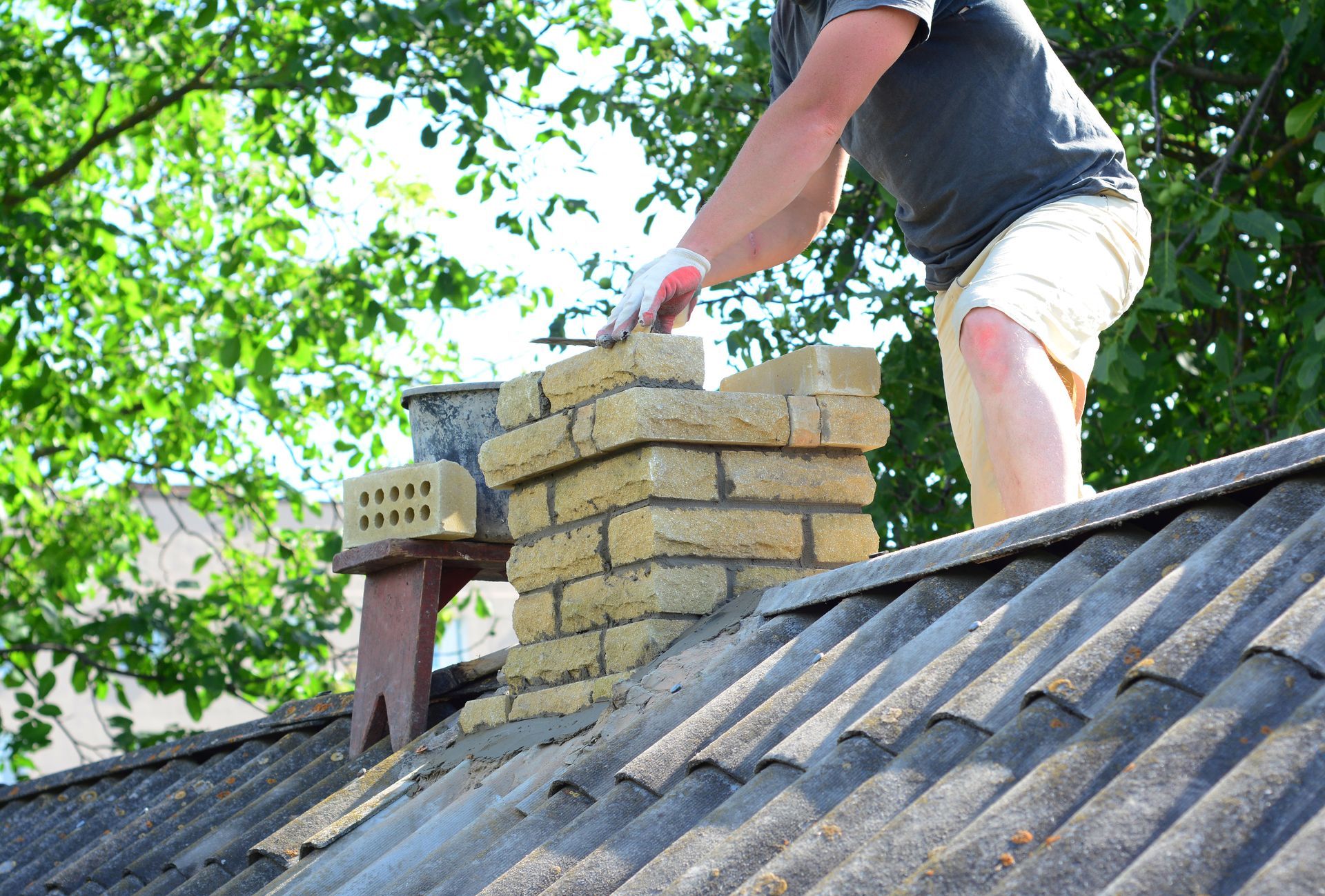 Professional masonry worker performing chimney tuckpointing on a residential brick chimney. Professional masonry worker performing chimney tuckpointing on a residential brick chimney.