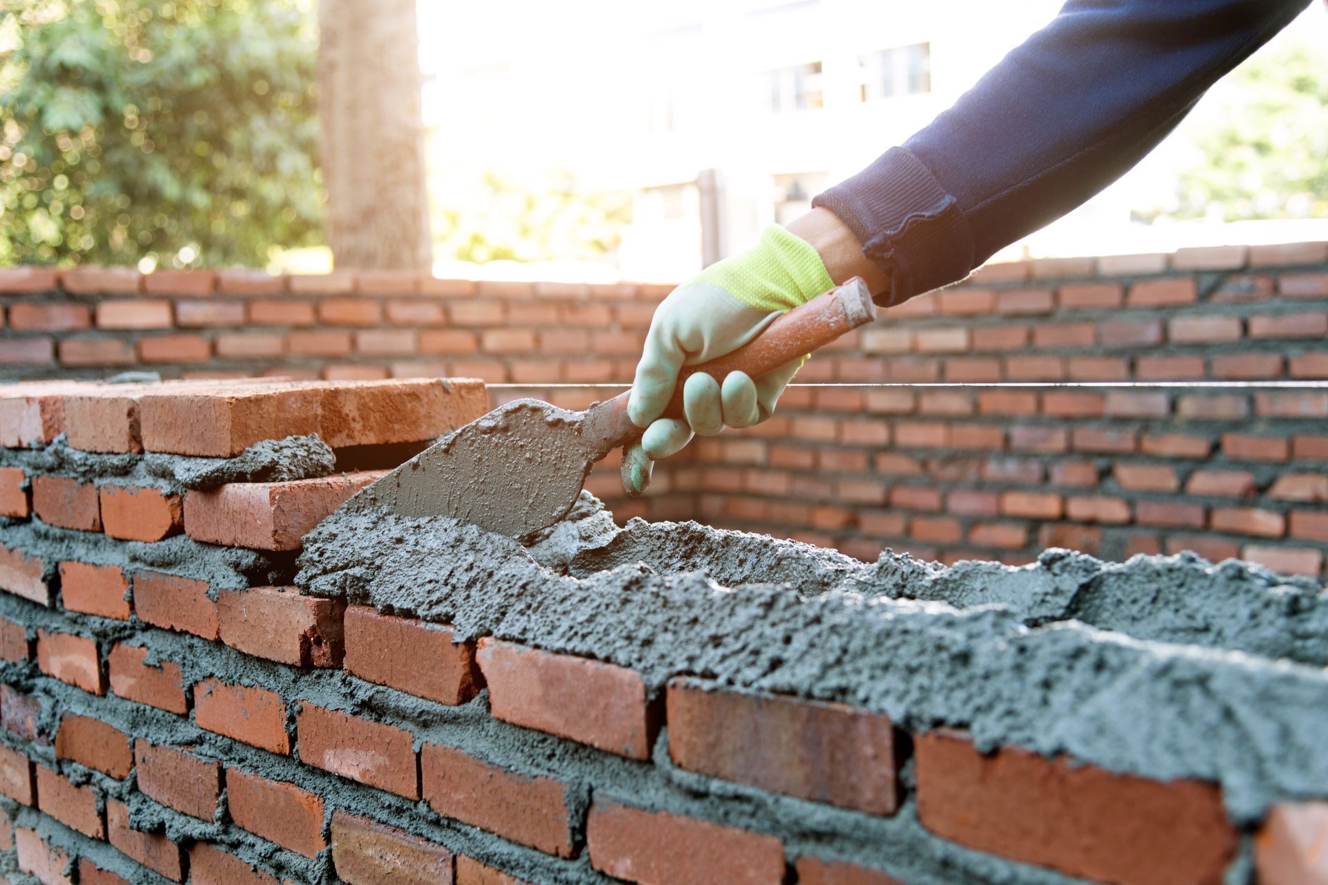 Gloved hand spreading wet mortar on a brick wall during construction