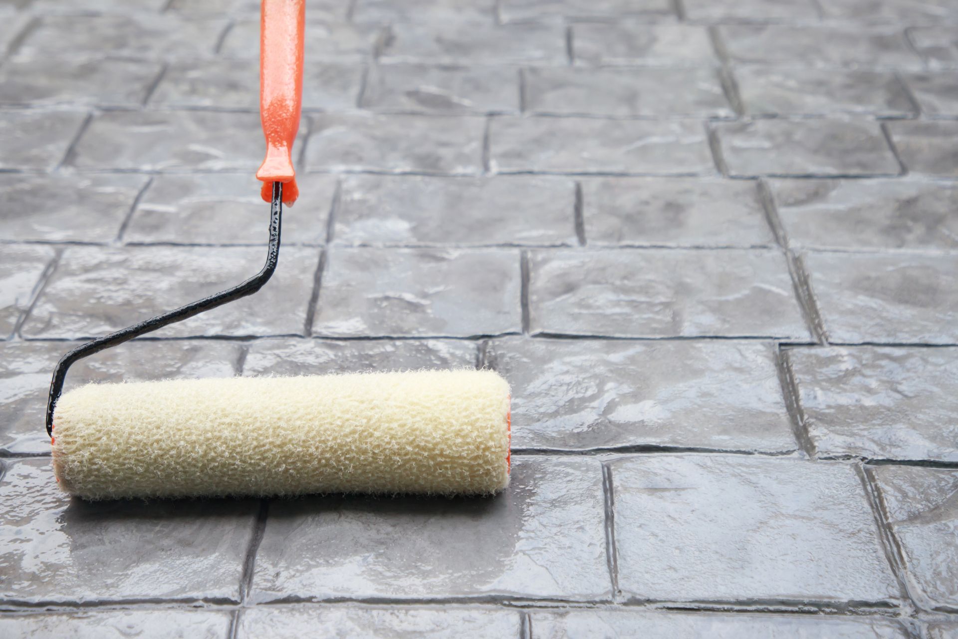 Paint roller with orange handle resting on wet gray stone pavement