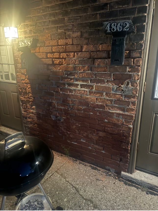 Brick wall with address 1862, mailbox, and grill. Dark red bricks lit by a lamp, outdoors.