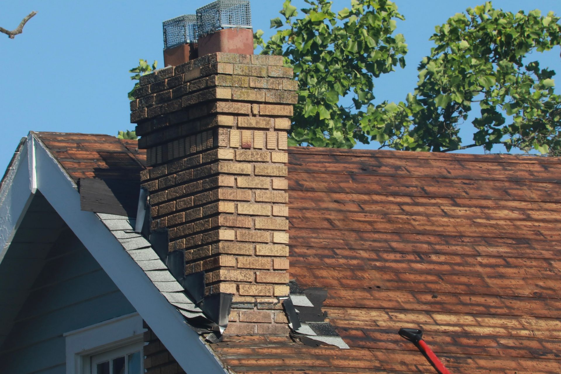 Brick chimney on a house roof with visible damage and missing shingles.
