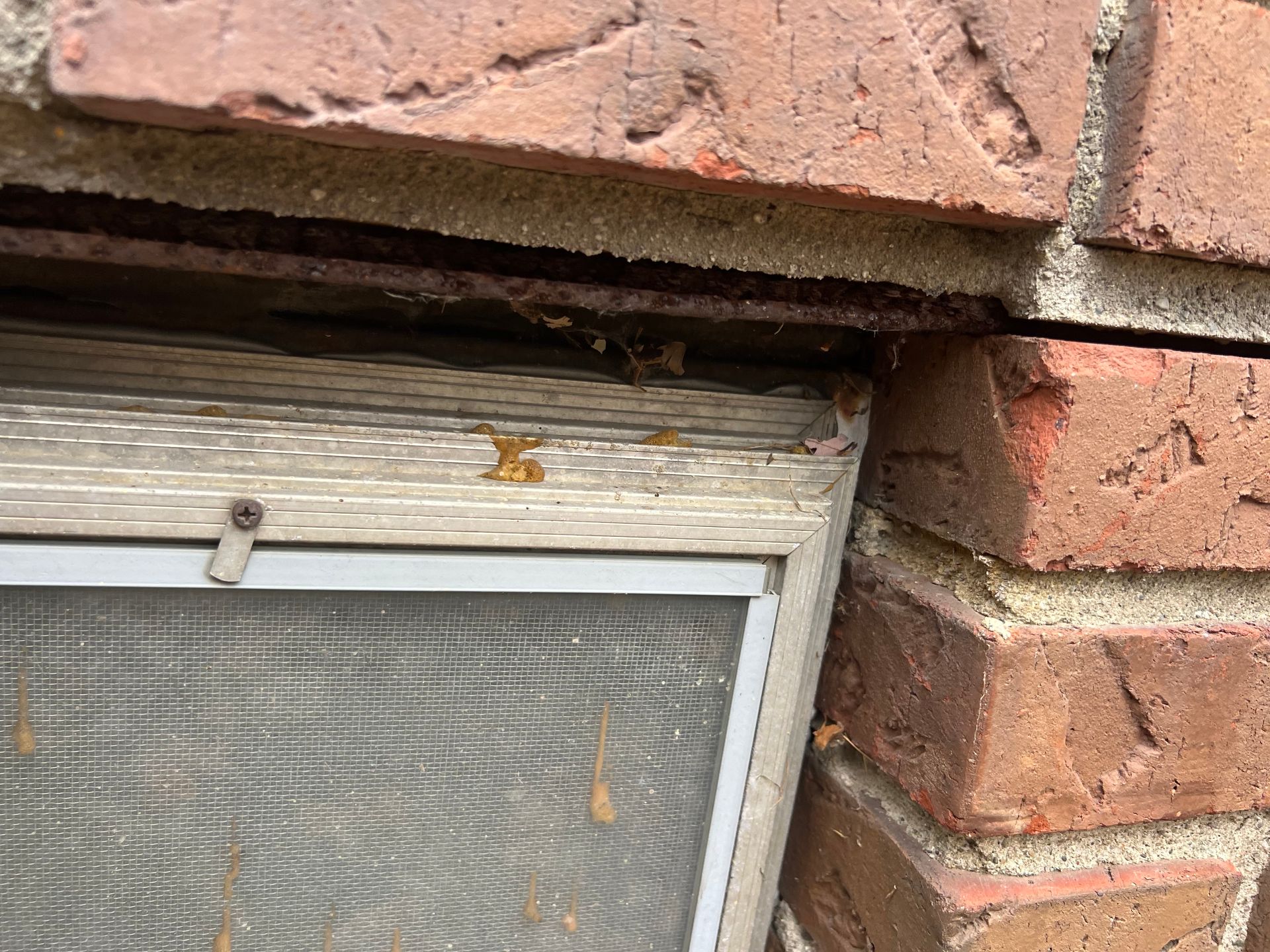 Damaged window frame under brick wall with a gap above the screen