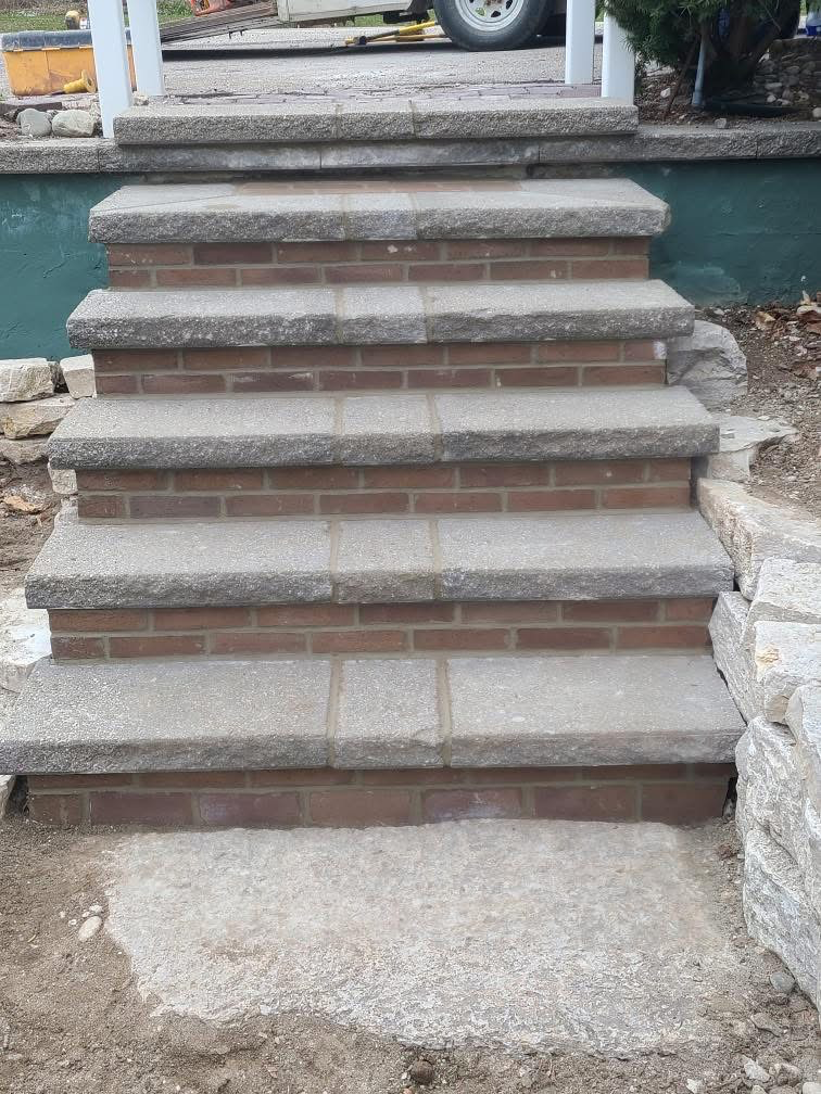 Concrete steps leading to a porch, bordered by stone and dirt on both sides
