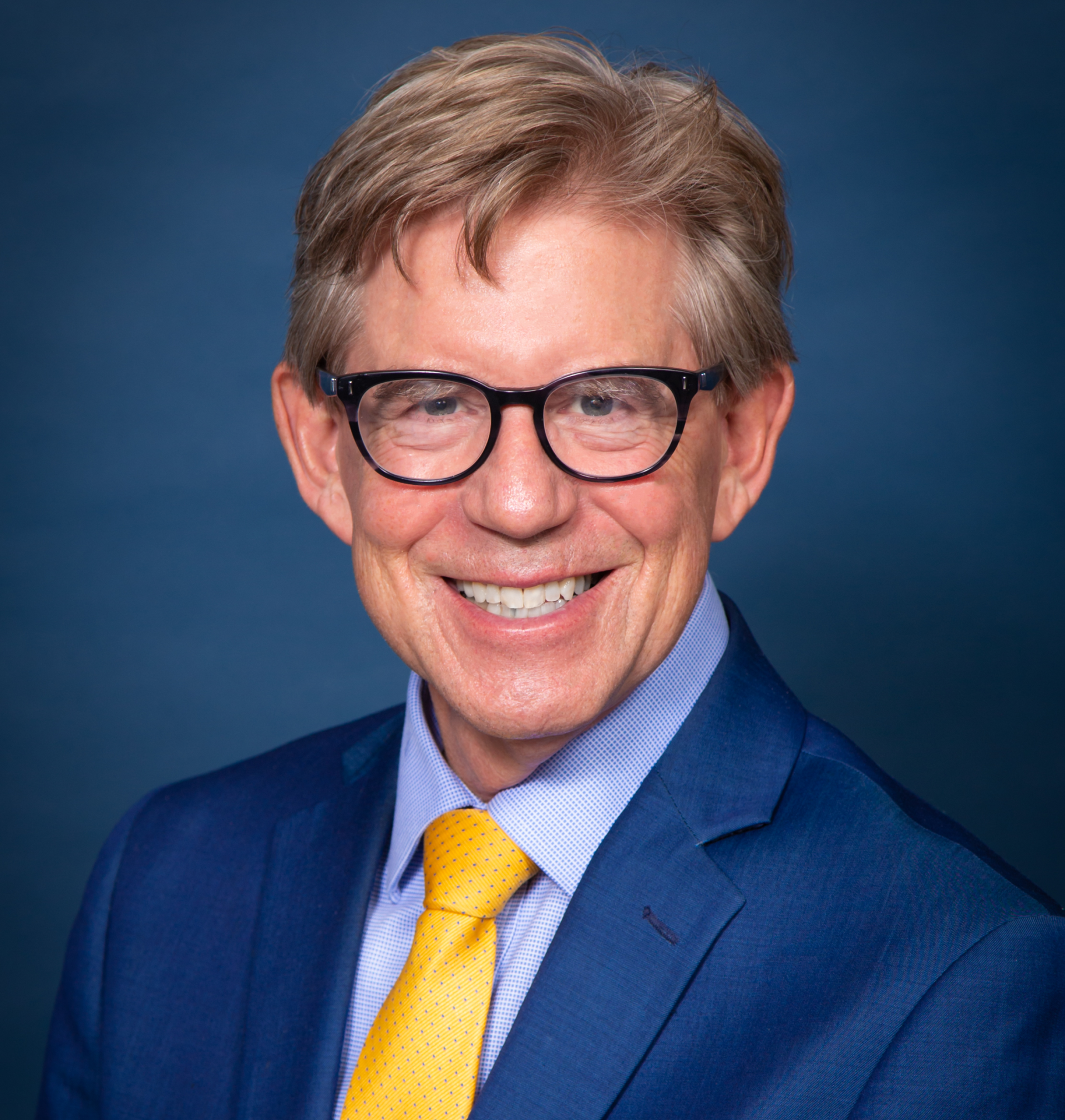 Smiling man in suit and glasses; blue background.
