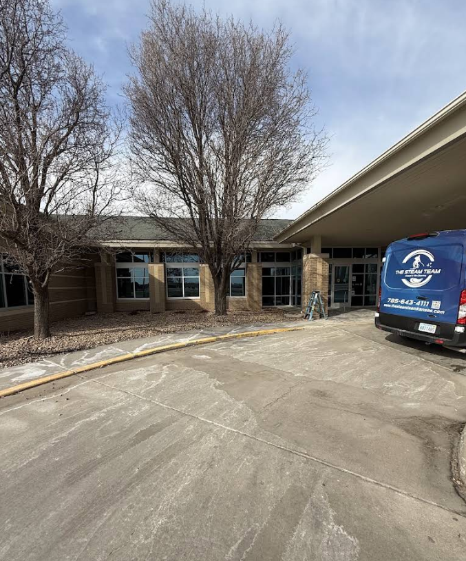 Covered building entrance with leafless trees and a blue service van parked by the curb.