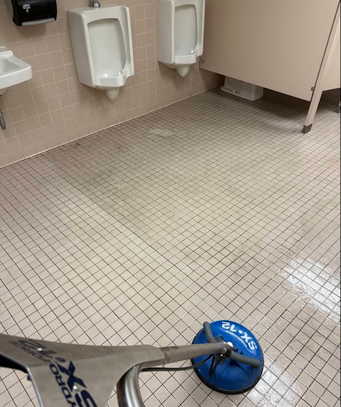 Restroom floor with urinals and a blue floor cleaning machine head in the foreground