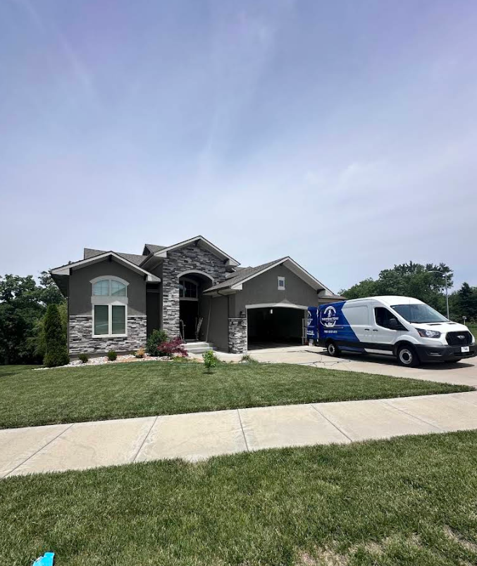 Suburban house with stone facade and garage, white van parked in the driveway, under a cloudy sky