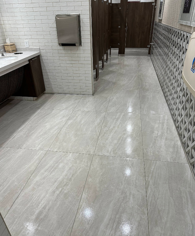 Bright restroom with tiled floor, sink on left, stall partitions ahead, and patterned wall on right