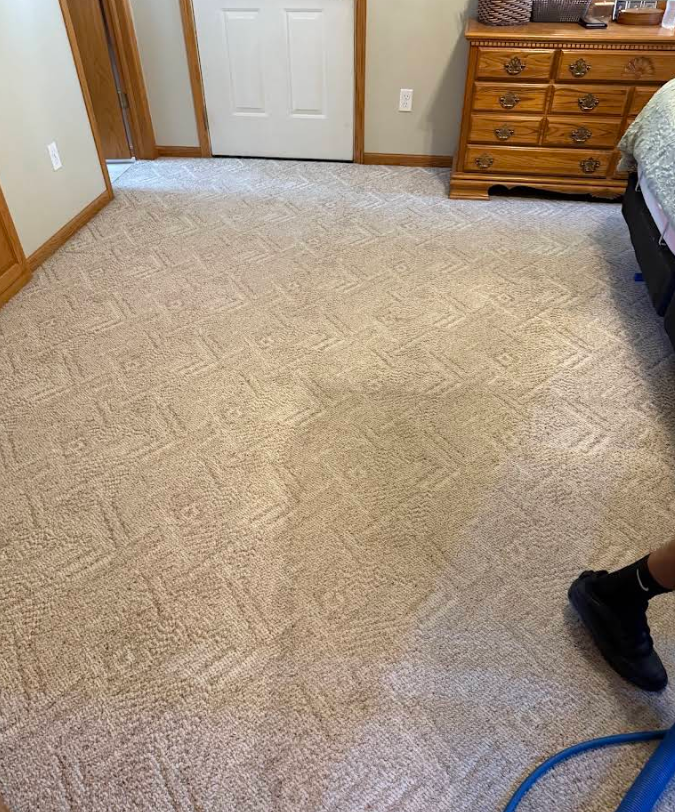 Carpeted bedroom with a white door, wooden dresser, and part of a person’s shoe and blue hose visible.