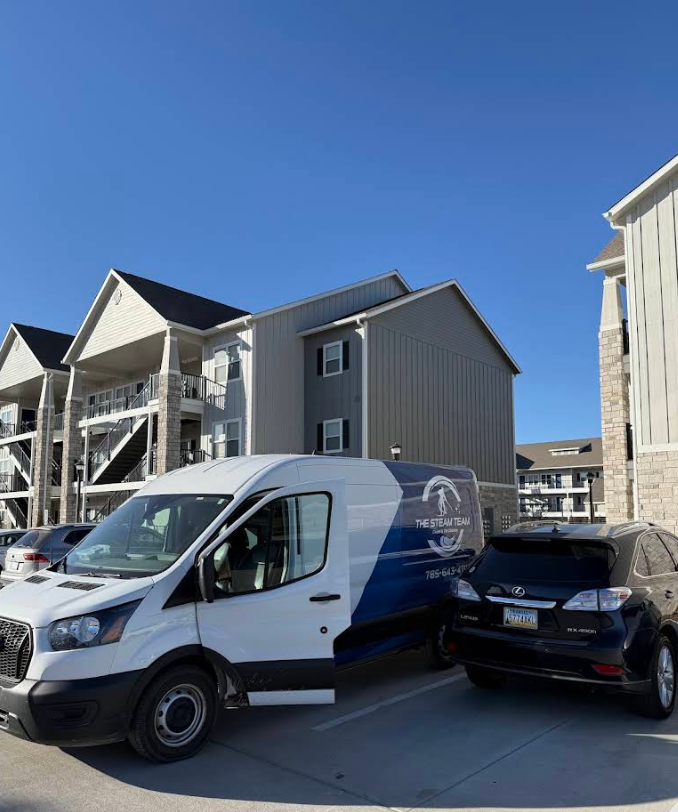 White service van parked beside a black SUV in front of townhomes under a clear blue sky