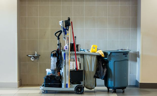 Custodial cleaning cart with mops and bins beside a wall-mounted water fountain in a tiled hallway