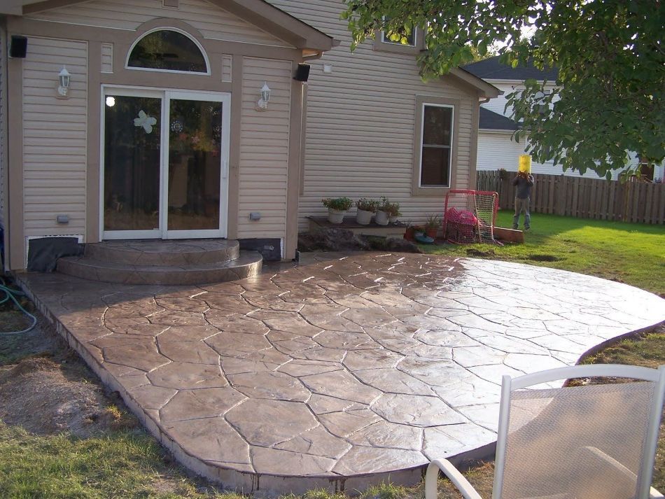 Stamped concrete patio next to a house with a curved edge and a sliding glass door.