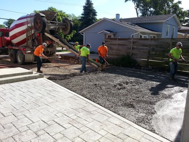 Construction workers pouring concrete from a truck into the driveway area, near a stamped concrete patio In Bensenville IL
