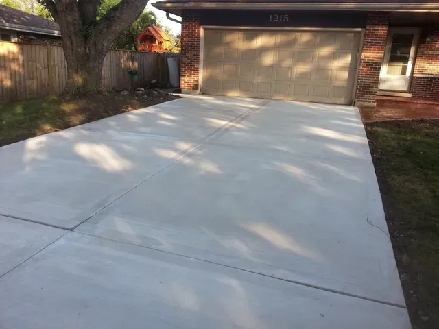 Newly poured concrete driveway in front of a brick house with a garage and a tree.