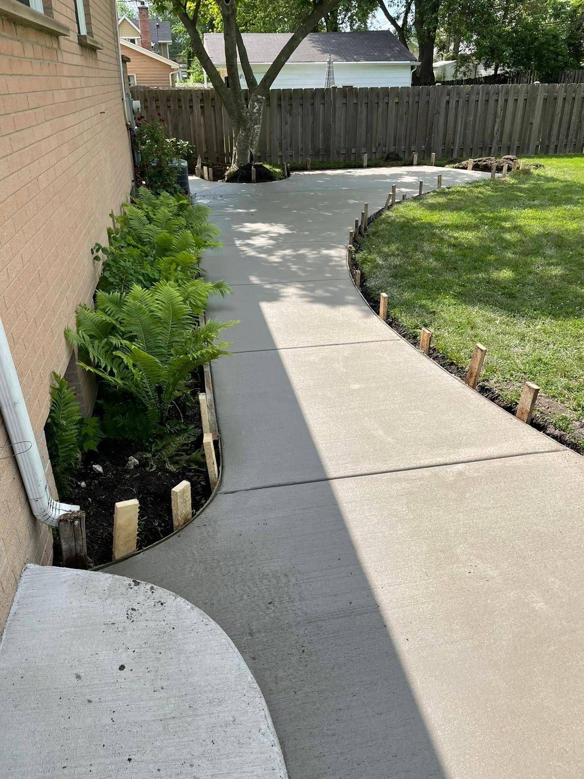 A concrete walkway leading to a backyard with a wooden fence.