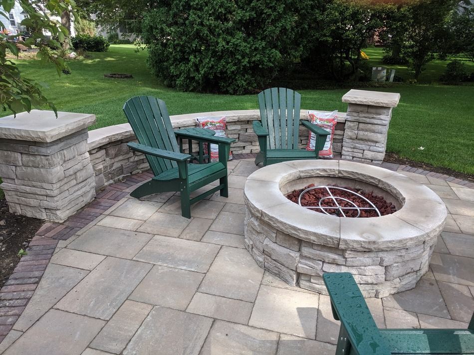Stone patio with fire pit, two green Adirondack chairs, and stone wall.