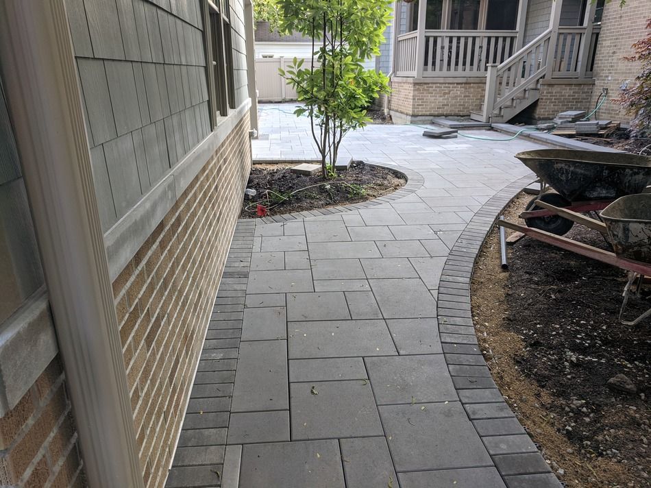 Brick walkway with a small tree and a curved path leading to a porch.